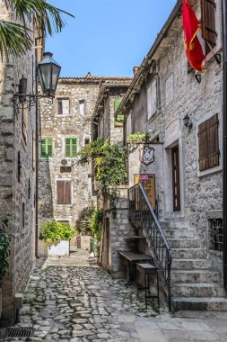 Geleneksel taş binaları ve üzerinde kırmızı Karadağ bayrağı asılı olan Kotor 'daki kaldırım taşı caddesi büyüleyici. Sessiz sokak yeşilliklerle süslenmiş ve tarihi mimariyi gözler önüne seriyor. Kotor, Karadağ - 18 Haziran 2021