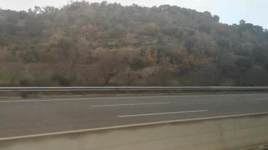 Otoyol boyunca uzanan orman tepeleri ile İspanya 'nın Katalonya kentindeki sonbahar manzaralarını bir otobüs penceresinden yansıtıyor. Video 27 saniye. Sakin kırsal bölge, yumuşak ve bulutlu bir gökyüzünün altından geçiyor.