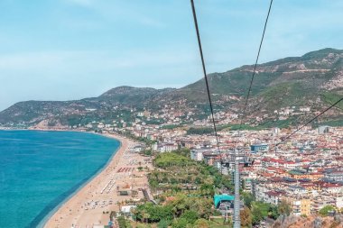 Türkiye 'deki Alanya Teleferik teleferik' in Kleopatra Plajı ve kentin kıyı şeridine bakan panoramik manzarası. Arkaplanda Akdeniz ve kıyı kentini çevreleyen yemyeşil dağlar yer alıyor.