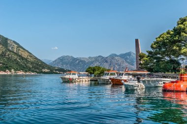 Tekneler arka planda dağlık manzaralarla birlikte sakin Kotor Koyu 'na demirledi. Sakin sular, doğanın güzelliğini yansıtıyor ve huzurlu bir manzara yaratıyor. Kotor, Karadağ - 18 Haziran 2021