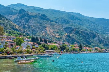 Kotor 'un sakin kıyı şeridi, turkuaz su boyunca yanaşmış tekneleri ve yemyeşil dağlardan oluşan bir zemin üzerine kurulmuş pitoresk evleri. Canlı manzara Adriyatik bölgesinin güzelliğini vurguluyor. Kotor, Karadağ - 18 Haziran 2021