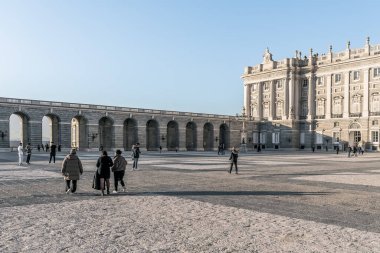 Güneşli bir akşamda Madrid Kraliyet Sarayı 'nın avlusunda yürüyen insanlar. Geniş plaza tarihi kemerler ve büyük mimari ile çevrilidir. Madrid, İspanya - 30 Kasım 2021