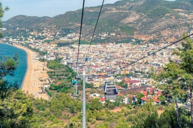 Türkiye 'nin Alanya kentinin hava görüntüsü, canlı kenti, Kleopatra Sahili ve yamaçtan yükselen teleferikleri gösteriyor. Akdeniz kıyı şeridi ve yemyeşil alanlar turizm ve keşif için manzaralı bir zemin oluşturuyor