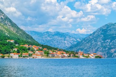 Karadağ 'ın Prcanj kentinde, geleneksel evler ve çevre dağların çarpıcı zeminiyle huzurlu bir manzara. Kotor Körfezi 'nin sakin suları manzaranın güzelliğini yansıtır.