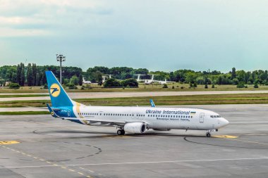 Kyiv, Ukrayna - 16 Haziran 2021: Boryspil Uluslararası Havaalanı 'ndaki UIA uçağı. Ukrayna Havayolları logosu olan uçak diğer araçlarla birlikte bir parkın arka planında duruyor.