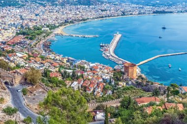 Türkiye 'nin Alanya kentinin panoramik manzarasında, Alanya Şatosu' ndan Kızıl Kule, marina ve Akdeniz yer alıyor. Sahne, canlı şehri ve sahil boyunca uzanan tarihi yapısını yakalıyor.
