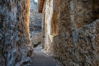 Türkiye 'nin Alanya Şatosu' nda sıcak güneş ışığıyla aydınlatılmış dar bir taş geçit. Antik mimaride engebeli taş duvarlar ve tarihin derinliklerine uzanan ahşap bir yol sergilenir.