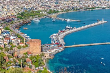 Kızıl Kule 'nin ve Alanya, Türkiye' deki limanın havadan görüntüsü. İkonik ortaçağ kulesi, canlı şehir binaları ve Akdeniz 'in turkuaz sularıyla çevrili hareketli marinanın yanında duruyor.