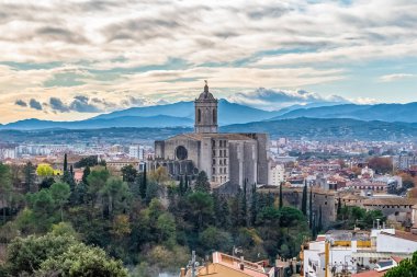 Girona 'nın panoramik şehir manzarası ön planda Saint Mary Katedrali ile çevrili, Akdeniz bitki örtüsü ve tarihi binalarla çevrili. Dağlar ve dramatik bulutlar İspanya 'nın kuzeydoğusundaki bu güzel Katalan şehrini çevreledi.