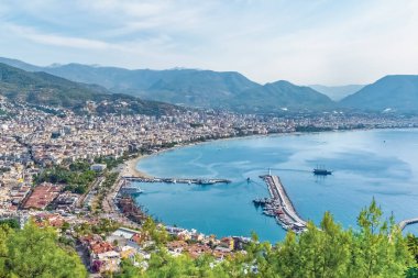 Alanya şehrinin manzarası ve yüksek görüş açısına sahip bir dağ manzarası. Huzurlu kıyı şeridi ve tekneler pitoresk bir Akdeniz atmosferi oluşturuyor.