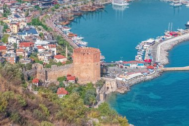 Türkiye 'nin Alanya kentindeki tarihi Kızıl Kule ve liman manzarası. Limana bakan ikonik yapı, tekneler, şehir binaları ve deniz manzarası ile çevrili.