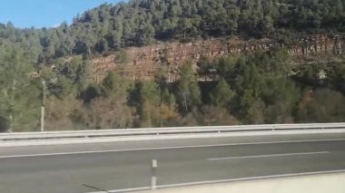 Lleida 'dan Girona, Katalonya, İspanya' ya giden otoyolda manzara otobüsü. Video 37 saniye. Pencereden çam ormanları ve sonbahar tepeleri. Açık gökyüzü ve kayalık yamaçlar yaklaşan trafik ile harmanlanarak dinamik bir manzara oluşturuyor.