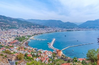 Türkiye 'nin Alanya kentinde ikonik Kızıl Kule ve limanla panoramik bir manzara. Sakin Akdeniz ve dağlık zemin manzaralı bir manzara yaratır.