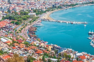 Alanya 'nın limanının havadan görünüşü gezinti güvertesi boyunca ve yakındaki kumsalda bulunan renkli korsan gemileriyle dolu. Hareketli kıyı bölgesi şehrin ve Akdeniz 'in güzel bir manzarasını sunuyor.