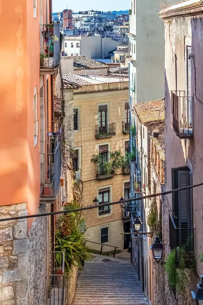 İspanya 'nın Girona şehrindeki Pujada de la Catedral' in dar taş merdivenleri, renkli tarihi binalar ve bitki süslemeli balkonlar arasında dönüyor. Büyüleyici ortaçağ sokak araları teras ve sokak lambalarıyla geleneksel İspanyol mimarisini gözler önüne seriyor.