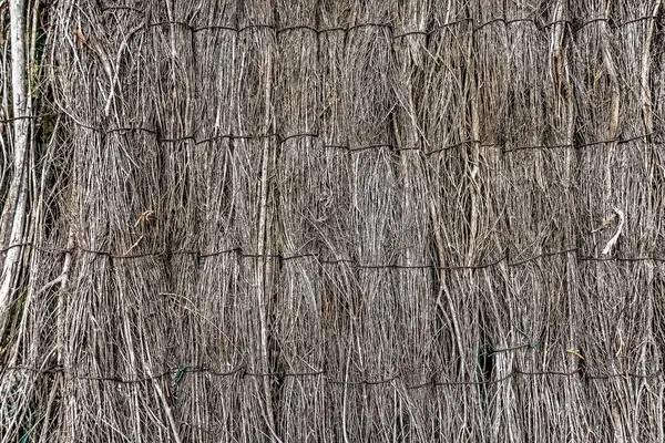 Geleneksel sazdan yapılmış çatı ya da duvar, doğal bir yalıtım dokusu yaratmak için yatay tel destekli sazlıktan yapılmış. Ayrıntılı yakın çekim, sürdürülebilir bir yapı malzemesi oluşturan saman iplikçiklerinin katmanlı düzenini gösterir