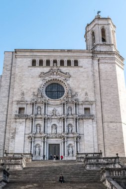 Süslü barok detaylarıyla Girona Katedrali 'nin görkemli cephesi, büyük taş merdiven, heykeller, dekoratif yuvarlak pencere ve açık mavi gökyüzüne karşı yükselen çan kulesi. Girona, İspanya