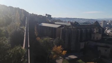 İspanya, Girona 'nın panoramik manzarası güneşli bir sonbahar sabahında antik kale duvarlarından. Video 20 saniye. Girona Katedral Kulesi ortaçağ çatıları ve dağ ufkuyla renkli şehir manzarasının üzerinde yükseliyor