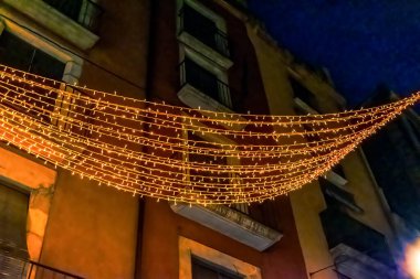 İspanya 'nın Girona kentindeki tarihi bina cephesinin Noel ışıkları süslemesi. Sıcak LED sicim lambaları, gece gökyüzüne ve geleneksel mimari arka plana karşı aydınlık tepe örtüsü oluşturur.