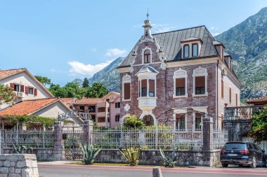 Kotor 'da güzel bir villa, ön bahçesinde metal çitleri ve agave bitkileri olan Akdeniz mimarisi sergiliyor. Ev, dağların manzaralı bir zeminine karşı duruyor. Kotor, Karadağ - 18 Haziran 2021