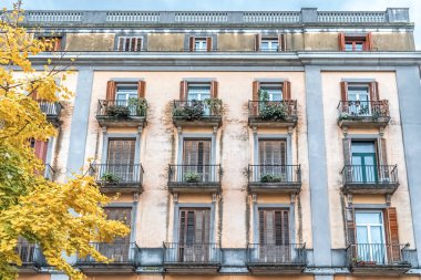 Placa de la Independencia 'daki bina cephesi, 18, Girona, İspanya. Balkonlar, panjurlar, çiçekler ve sonbahar renkleri mimariyi vurguluyor