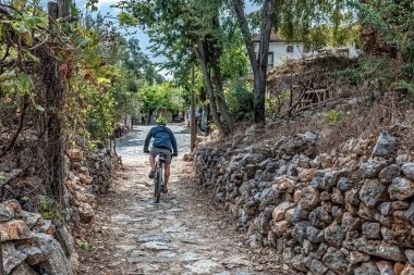 Türkiye 'nin Alanya Şatosu' ndaki ağaçlar ve taş duvarlarla çevrili taştan bir patikadan geçen bir bisikletçi. Sessiz atmosfer, ortaçağ bölgesinin manzaralı ve tarihi cazibesini artırıyor. Alanya, Türkiye - 24 Ekim 2020