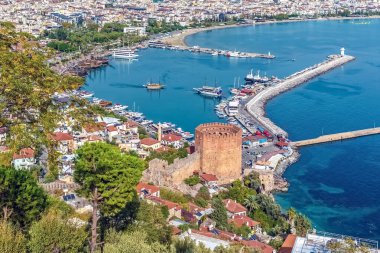 Alanya 'nın tarihi Kızıl Kulesi ve limanın manzaralı Akdeniz kıyılarıyla çevrili panoramik manzarası. Canlı şehir manzarası derin mavi deniz ve yemyeşil ile çelişiyor.