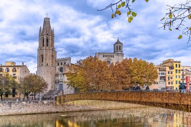 Saint Feliu Bazilikası ve sonbahar mevsiminde Onyar nehrine yansıyan Noel ışıklarıyla aydınlatılmış köprü. Renkli evler ve sonbahar yaprakları pitoresk şehir manzarası yaratır. Girona, İspanya - 27 Kasım 2021