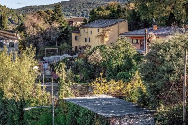 İspanya 'nın Girona kentindeki Katalonya dağlarının eteklerindeki yemyeşil bitkilerin arasına yuva yapmış kır evleri. Terasotta çatıları olan Akdeniz kır evleri bahçeler ve doğal yeşillikler ile çevrili tipik İspanyol konut mimarisi.