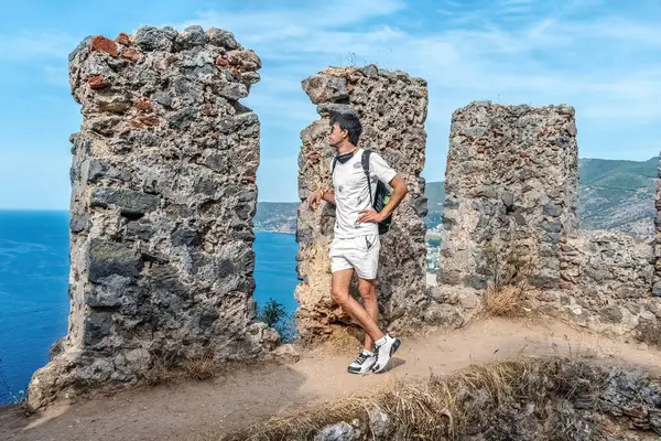 Alanya Kalesi 'nin taş kalıntıları arasında duran ve arka planda Türkiye' nin Akdeniz manzaralı adamı. Bu an hem sitenin tarihi atmosferini hem de manzaralı kıyı manzarasını yakalar.