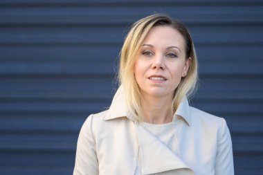 Orta yaşlı çekici bir sarışının portresi. Mavi bir duvarın önünde nazikçe gülümseyen bir kadın.