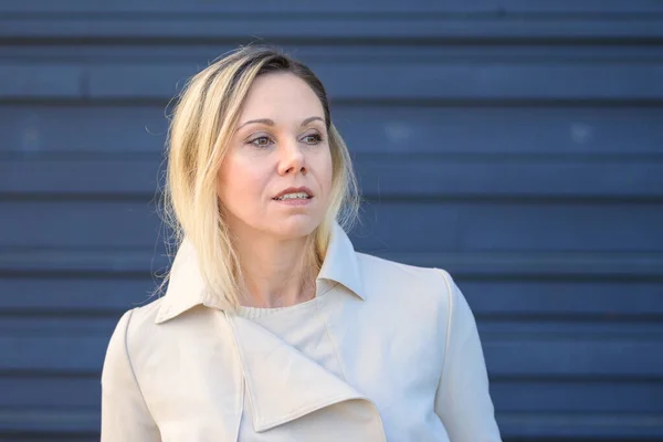 stock image Portrait of an attractive middle-aged blonde woman looking thoughtfully to the side in front of a blue wall