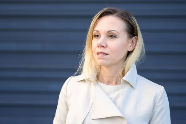 stock image Portrait of an attractive middle-aged blonde woman looking thoughtfully to the side in front of a blue wall