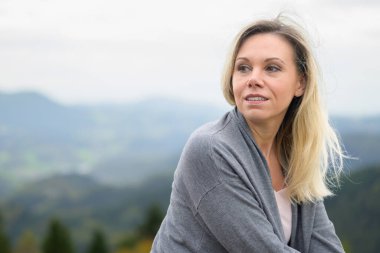 Orta yaşlı mutlu bir sarışının portresi omzunun üzerinden bir dağın tepesine ve sise bakıyor.