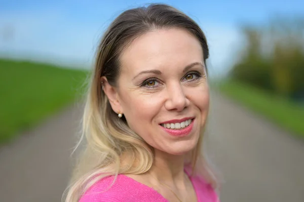 stock image Close up portrait of a gorgeous woman with pink lipstick and pink sweater in front of a road or trail looking over her shoulder in autumn