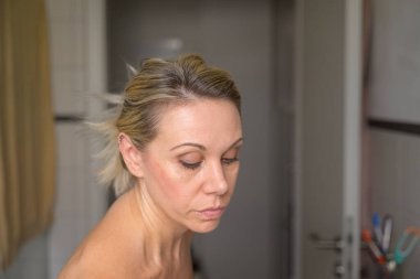 Orta yaşlı sarışın kadın sabah abdesti sırasında yüzünü banyoda temizliyor.