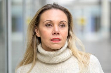 Beyaz balıkçı yaka kazaklı, çekici, orta yaşlı bir kadının portresi. Şehirde parlak beyaz bir arka planda düşünceli bir bakışla duruyor.