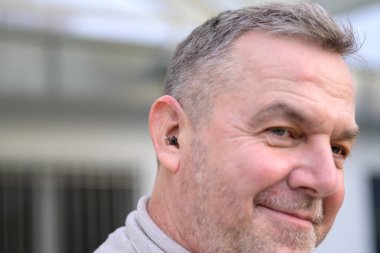 Side view of a middle aged gray haired hard of hearing man in his fifties or sixties with a hearing aid in his ear