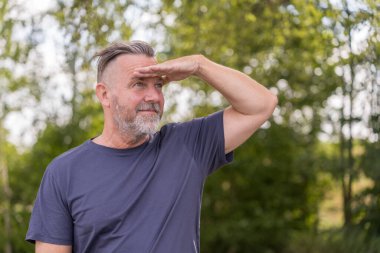 Pensive middle aged man with his hand to his forehead looking into the distance outside against a green background