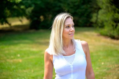 Attractive middle aged blond woman with long blond hair walking in a park in summer