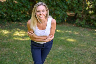 Blond woman leaning to the camera as she clasps her chest looking aside with a quiet smile