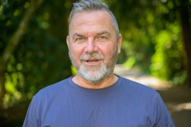 Son sınıf öğrencisi, dışarıda parkta, yüzünde beklenen ifadeyle kameraya bakıyor.