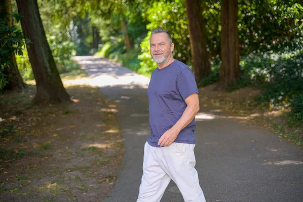 Stock image Middle aged bearded man walking in a shady rural lane turning to smile at the camera