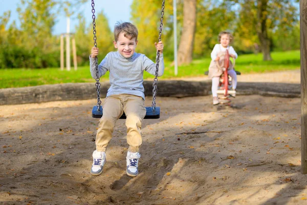 Salıncakta bir oğlan ve çocuk parkında arka planda bir kız