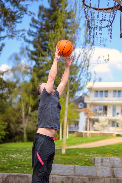 穿着黑色短裤的中年男子在运动场打篮球时跳投篮筐 — 图库照片