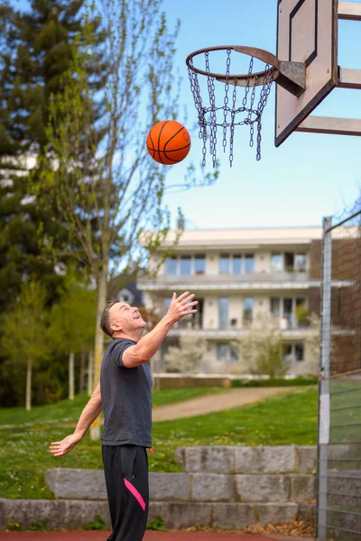 身穿黑色运动短裤的中年男子把篮球扔到运动场上 — 图库照片