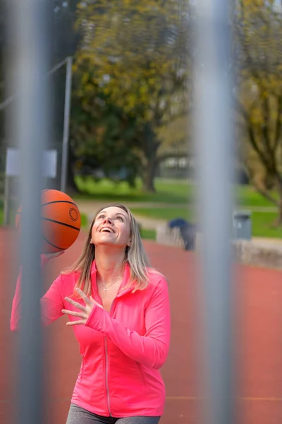一个迷人的金发女人正要跳起来 手里拿着篮球 在运动场上大笑不止 — 图库照片