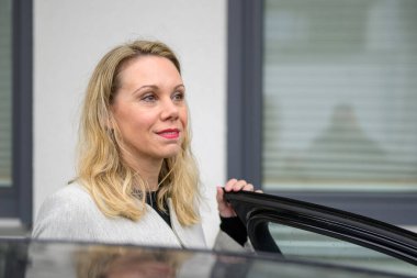 Orta yaşlı bir kadın arabaya binerken yan yana bakar.