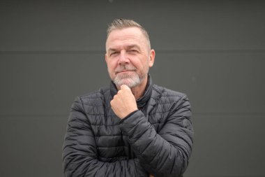 Orta yaşlı bir adam çenesini tutup kameraya bakıyor.