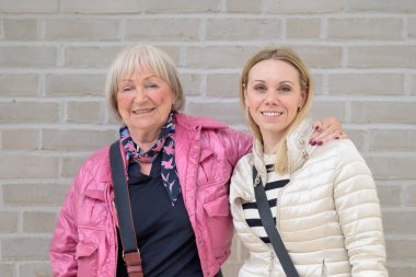 Anne ve kızı, beyaz bir duvarın önünde birbirlerini kollarıyla tutuyorlardı.